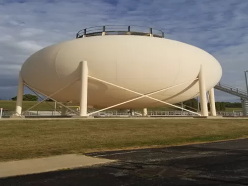 Large, white, spheroid water tower supported by white pillars on a grassy area with a staircase leading to the top.