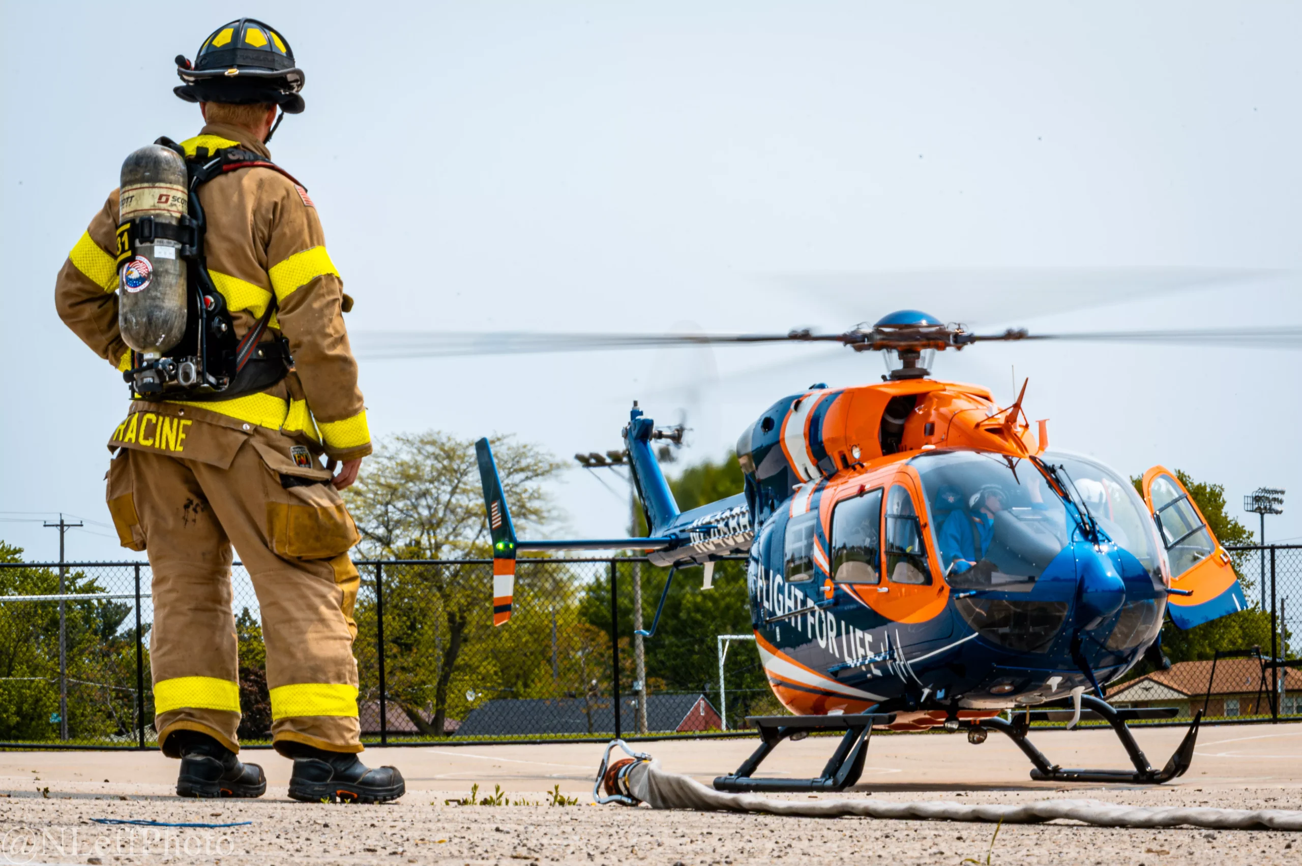 Firefighter in gear stands near a medical helicopter on a landing pad, preparing for emergency transport.