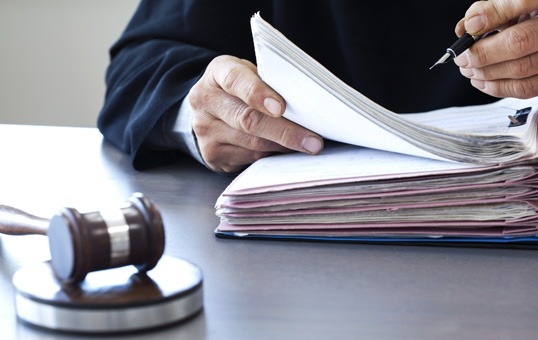 Judge in robes reviews legal documents with gavel on desk, symbolizing legal process and judicial review.