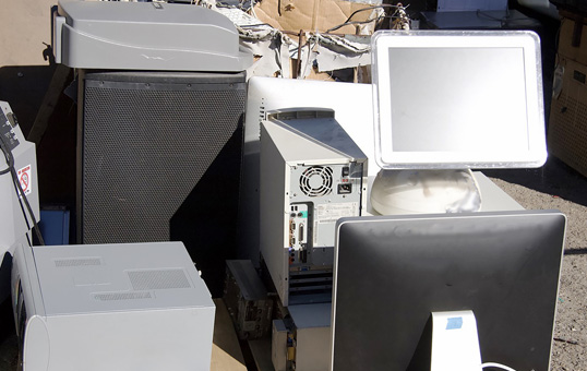Pile of discarded computer equipment including monitors, towers, and printers, suggesting e-waste or recycling.