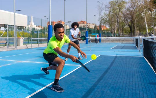 Two men playing pickleball on a blue outdoor court, one hitting the ball with his paddle.