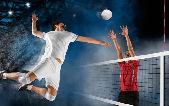 Volleyball player in white shirt jumps to spike ball over net; opponent in red shirt attempts to block.