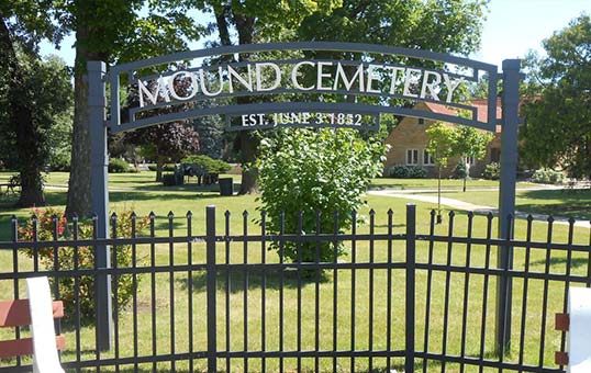 Mound Cemetery entrance sign, established June 3, 1882, with wrought iron fence and green landscape.