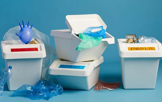 Three recycling bins labeled for different materials against a blue background, promoting waste sorting.