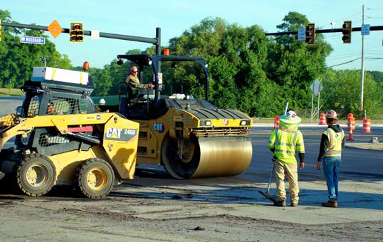 Road construction crew working with heavy machinery at an intersection with traffic lights.