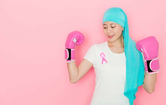 Woman in boxing gloves and headscarf with pink ribbon, symbolizing breast cancer awareness and fighting spirit.