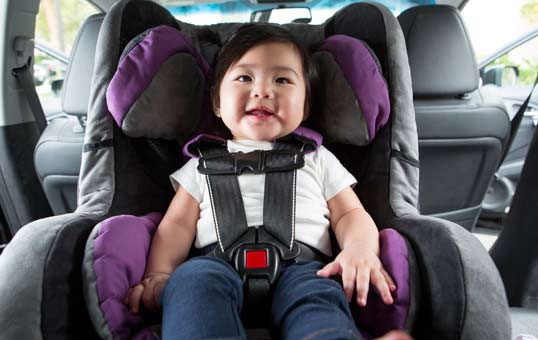 Happy baby secured in a forward-facing car seat with a five-point harness inside a vehicle.