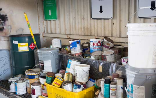 Collection of paint cans and containers at a recycling center, ready for processing and disposal.