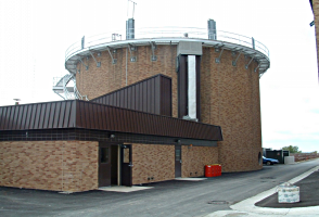 Exterior view of a circular brick water treatment facility with metal accents and a rooftop platform.