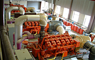 High-angle view of large, orange industrial engines with pipes in a power plant or factory setting.