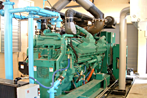 Large green industrial generator with blue pipes and black ventilation hoses in a utility room.