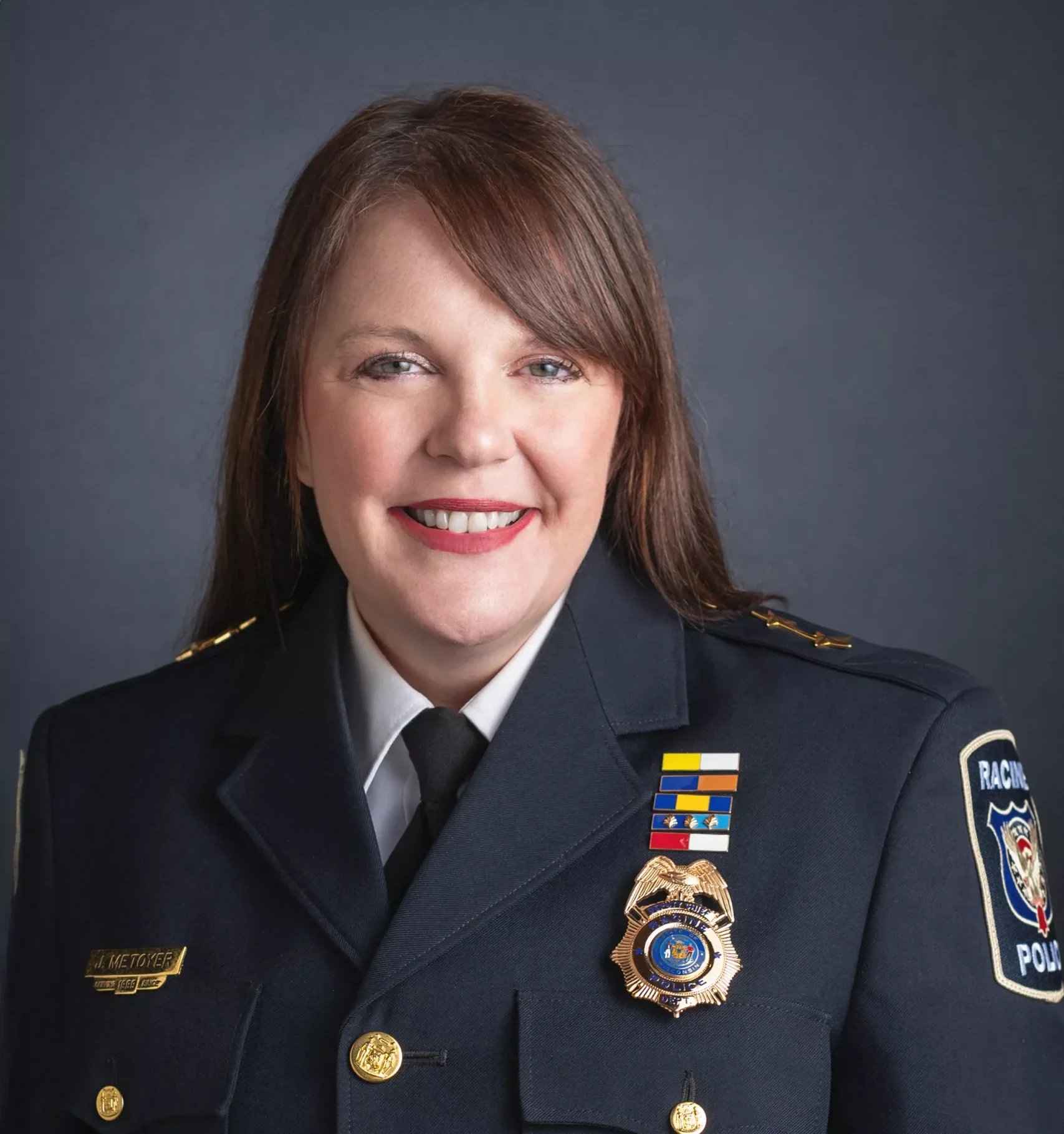 Portrait of Maureen Wallner, Racine Police Chief, in uniform smiling against a gray background.