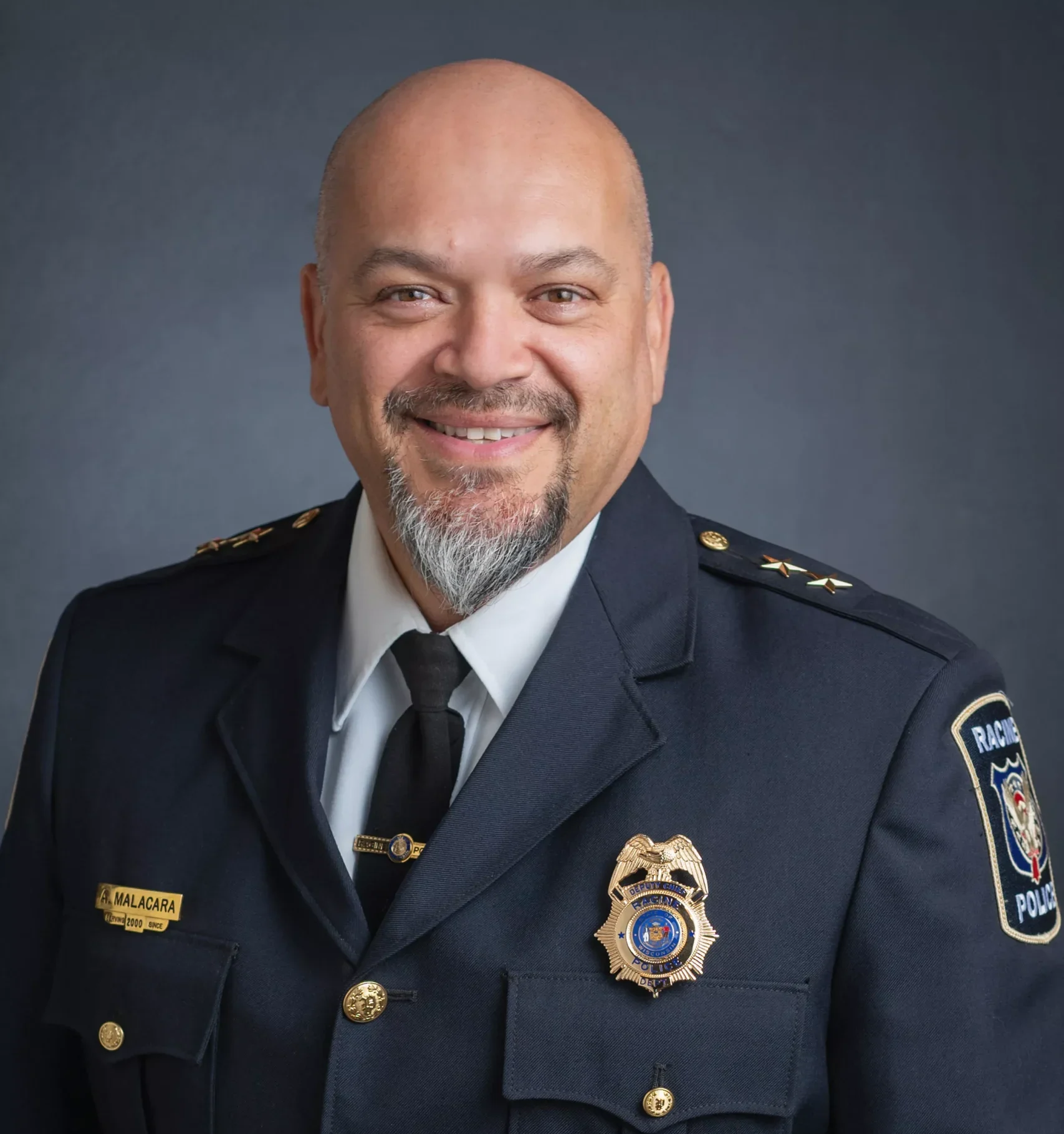 Headshot of Racine Police Chief Maurice A. Chappee in uniform, smiling against a dark gray background.