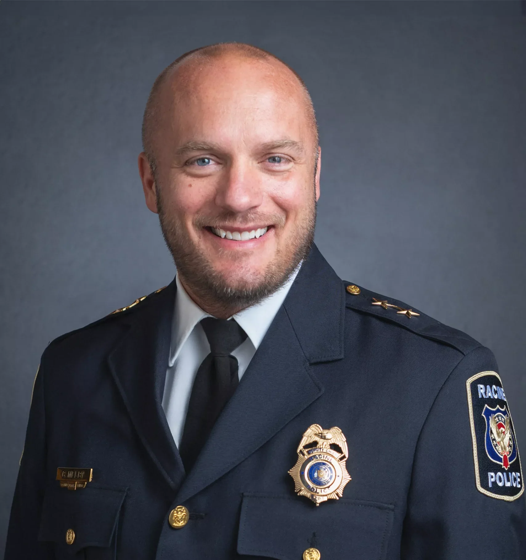 Headshot of Racine Police Chief Maurice Robinson in uniform, smiling against a gray background.