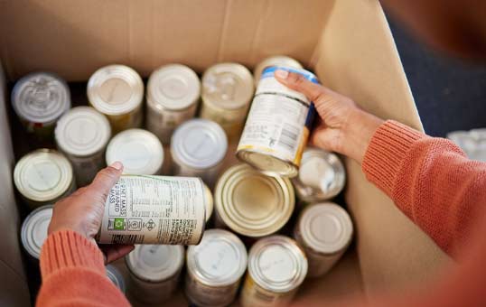 Hands sorting canned goods in a cardboard box, likely for donation to a food bank.
