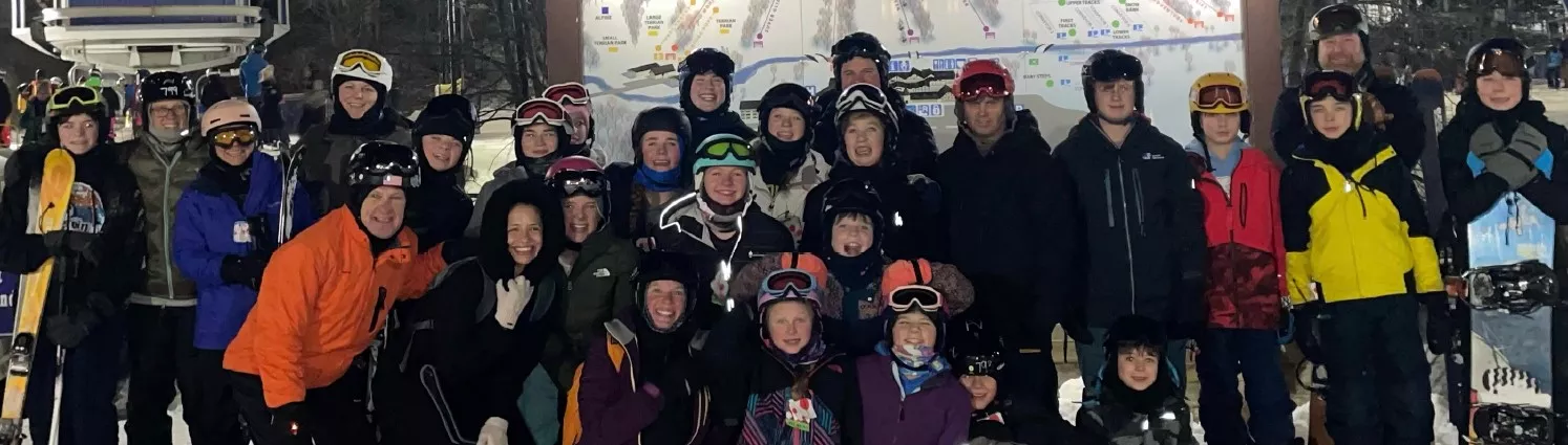 Group of skiers and snowboarders in winter gear pose for a photo in front of a trail map.