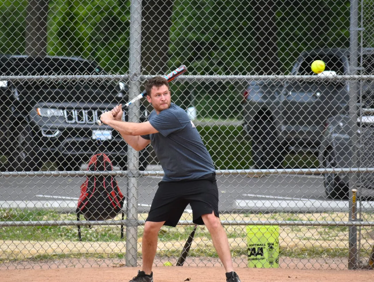 Man batting during a softball game, preparing to swing at a yellow ball.
