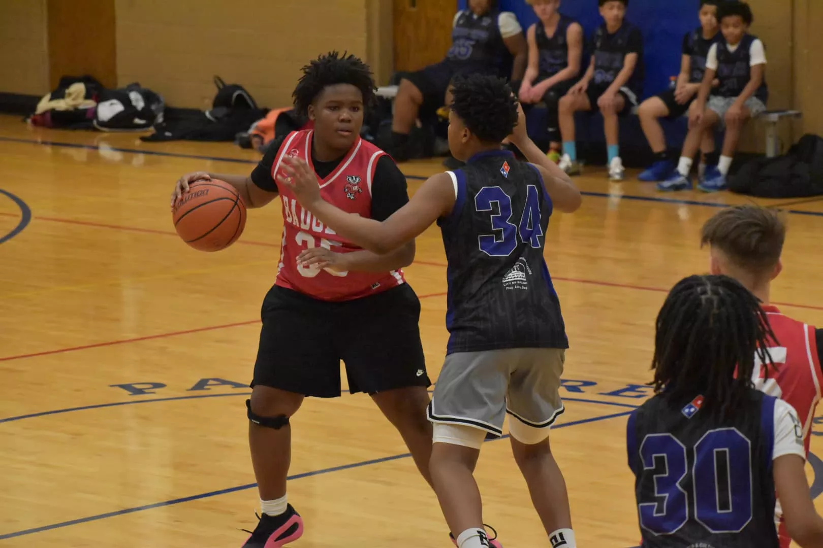 Basketball player dribbles ball while defended during a game. Players wear jerseys with numbers.