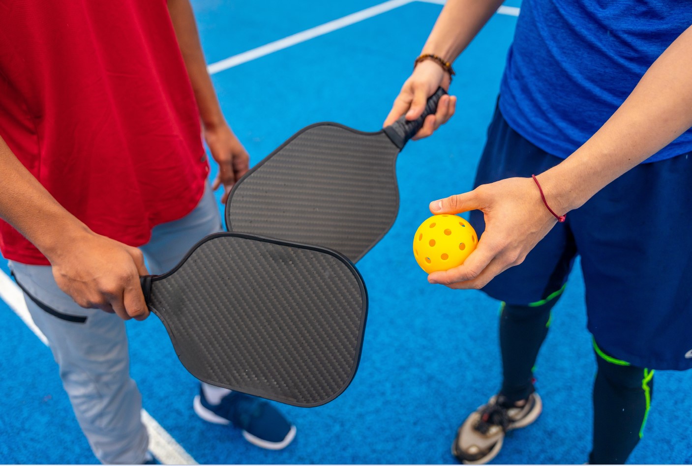 Two people holding pickleball paddles and a yellow ball on a blue court, ready to play.