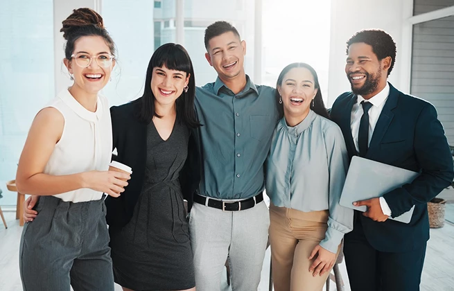 Group of five diverse, smiling professionals in an office setting, conveying teamwork and a positive work environment.