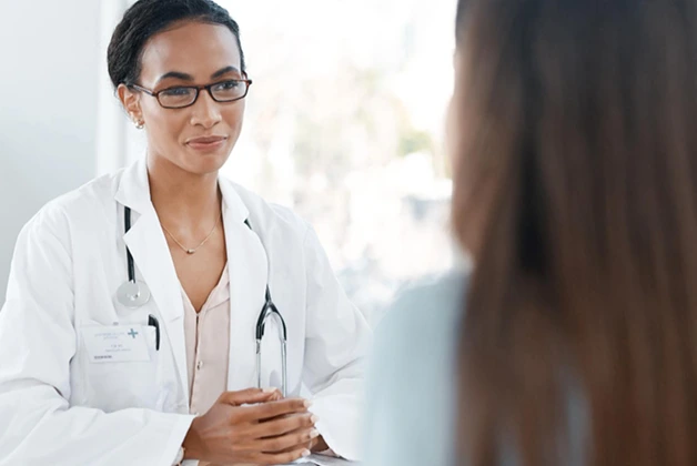 Doctor in white coat with stethoscope consults with patient. Focus on doctor, patient is blurred.