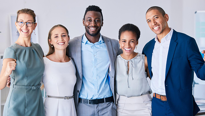Diverse group of five smiling professionals in business attire, standing shoulder-to-shoulder in an office setting.