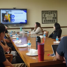 Group of people seated around a conference table watching a presentation on a large screen.