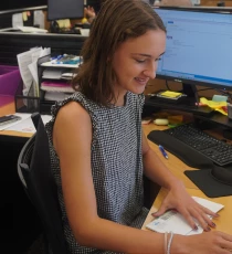 Woman at desk opening envelope, with computer and office supplies in background.
