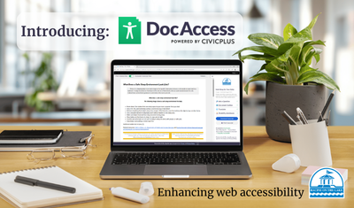A photo of a laptop computer with a PDF document displayed on the screen, sitting on a wooden desk surrounded by office supplies. The words Introducing Doc Access and Enhancing web accessibility are displayed. The City of Racine logo is in the bottom corner.