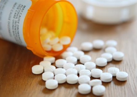 A tipped orange pill bottle in the background with round, white pills spilling out onto a surface.