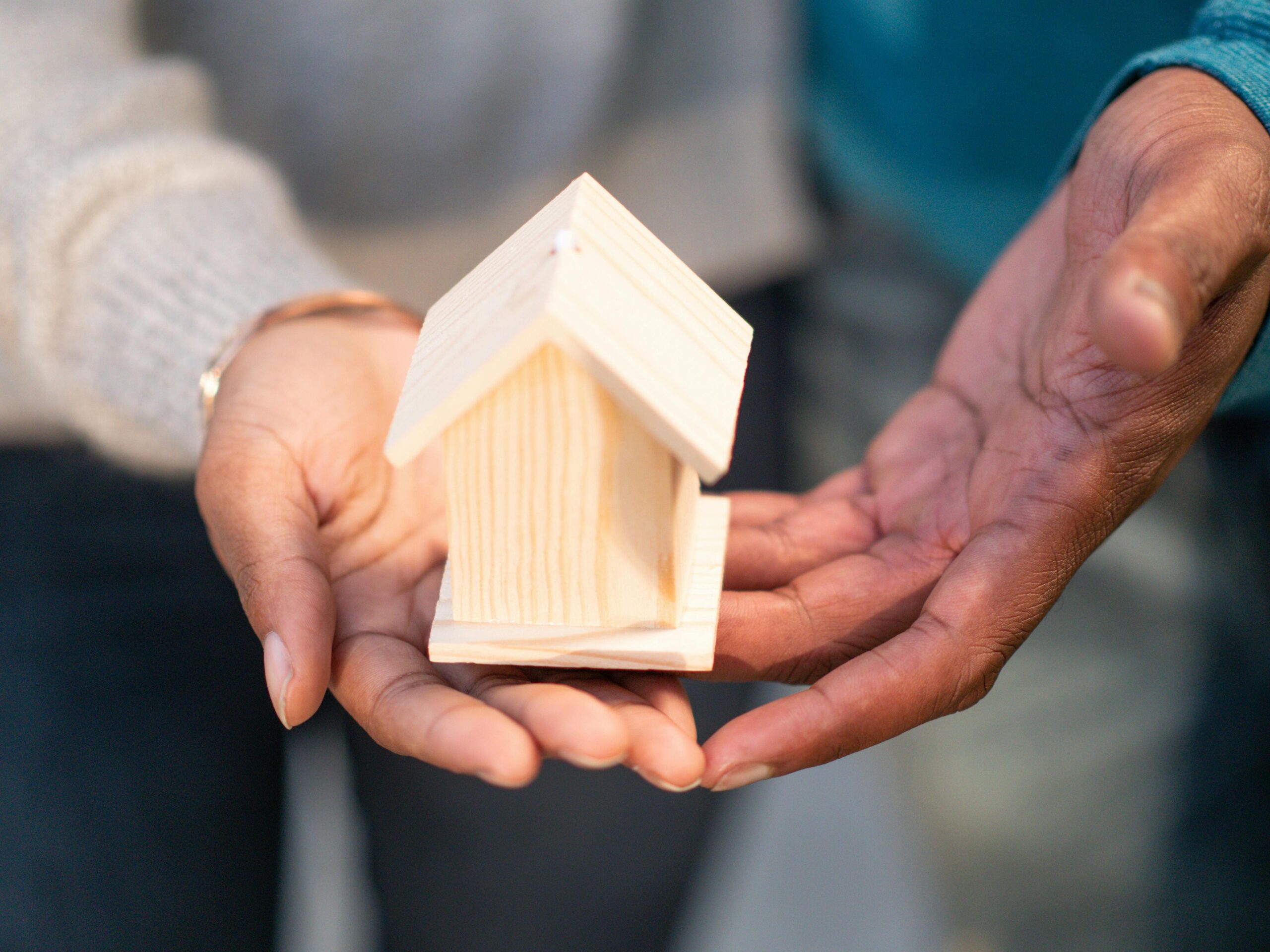 Hands of diverse people holding a small wooden house as a symbol of fair housing.